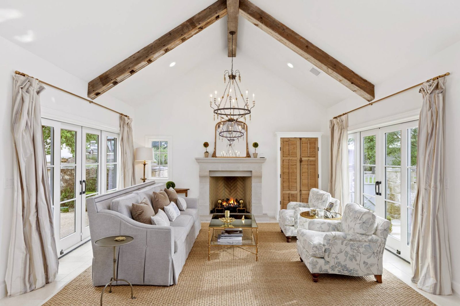 French Country custom home living room with vaulted wood beam ceiling herringbone fireplace and designer furniture by luxury home builder 919 Custom Homes TX